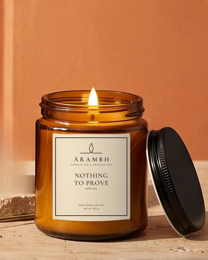 A lit Nothing to Prove candle with the ĀRAMBH label on a travertine step